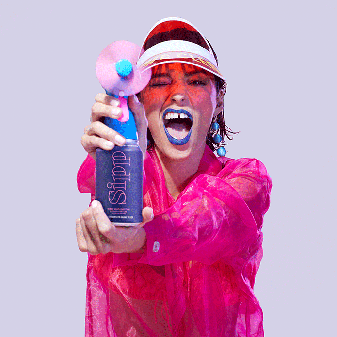 Woman in pink windbreaker and translucent visor holding out a spray bottle fan attached to a can of Sipp